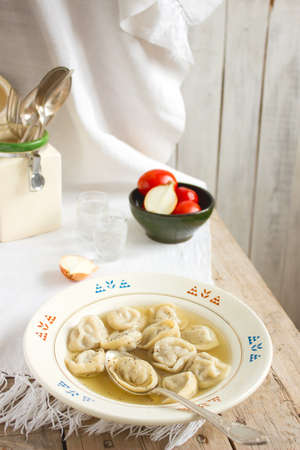Pelmeni with broth on a wooden table with a snack and vodka.の写真素材