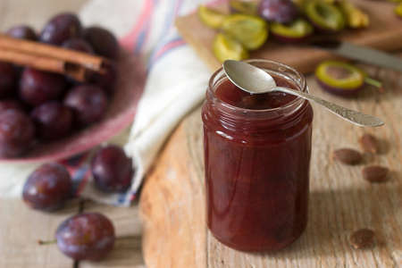 Homemade plum jam or confiture in a glass jar, and fresh plums on a wooden background. Rustic style, selective focus.の写真素材