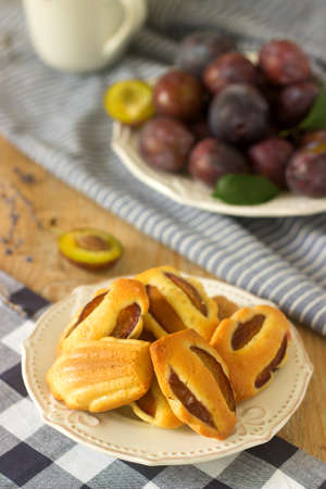 Madeleine with plums and plums. French cookies. Rustic style, selective focus.