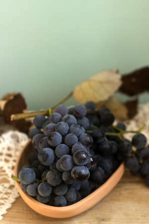 Grapes in a clay plate on a wooden background. Rustic style, selective focus. Vertical.の写真素材
