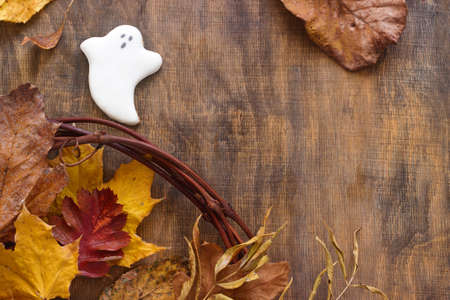 Gingerbread ghost for halloween, decorated with autumn leaves, on a wooden background. Selective...