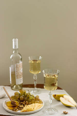 Glasses with white wine and a bottle of wine with a snack - cheese, walnuts and grapes. Rustic...