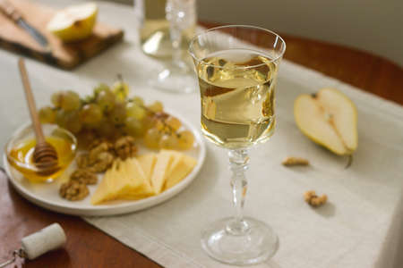 Glasses with white wine and a bottle of wine with a snack - cheese, walnuts and grapes. Rustic style.の写真素材