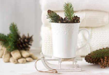 Winter concept with white blanket pullover, gloves, sleds, cup, cones and fir branches. Selective...
