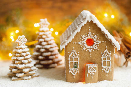 Gingerbread house and Christmas trees on a luminous background. Bokeh effect, selective focus.
