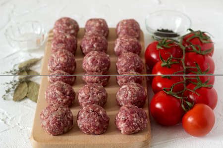 Raw meatballs, tomatoes and spices on a white concrete background. Rustic style, selective focus.