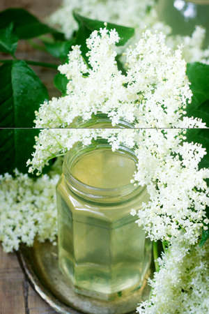 Homemade syrup of elderberry flowers in a glass jar and elder branches on a wooden table Rustic style.の写真素材