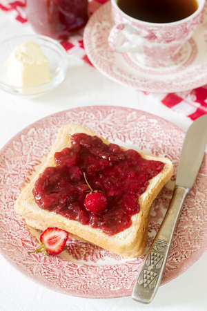 Breakfast of bread toasts with butter and strawberry-rhubarb jam, served with tea. Rustic style,...