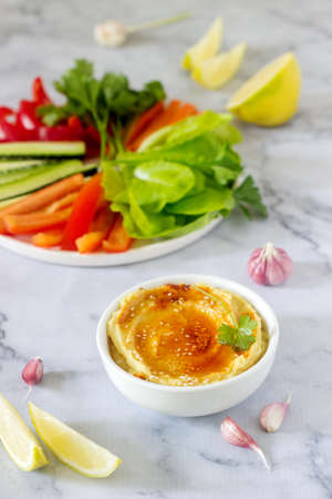 Hummus, different vegetables and lettuce leaves with lemon and garlic on a light background. Vegan...