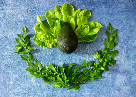 Fresh ripe avocado and various herbs, lettuce, basil, parsley and spinach on a blue background....