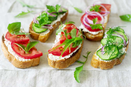 Bruschetta or sandwiches with tomatoes, cucumbers and cream cheese, decorated with greens. Selective focusの写真素材