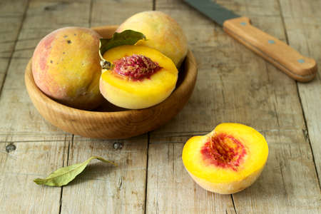 Three ripe velvet peaches in a wooden bowl on a wooden background. Rustic style, selective focus.