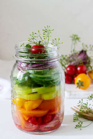 Salad of vegetables with herbs in a glass jar and fresh vegetables on a table. Selective focus.の写真素材