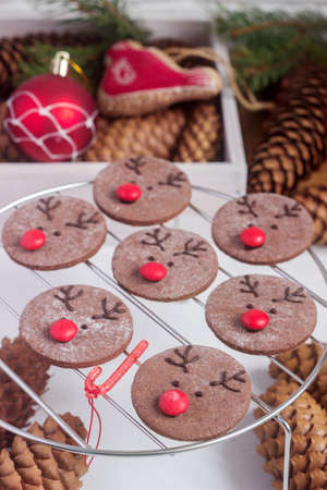 Chocolate festive cookies in the form of a deer Rudolph with a red nose surrounded by festive decor. Selective focus.の写真素材