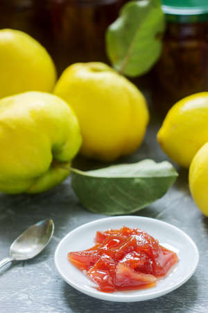 Quince jam on a white saucer, quince fruits and jars of jam on a gray background. Selective focus.の写真素材