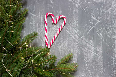 Winter background with fir branches, garland and candy canes on a gray concrete background. Greeting...