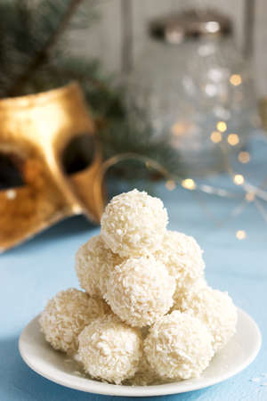 Coconut candies on a winter background with a garland, a candle and fir branches. Selective focus.