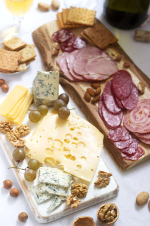 Appetizer of various types of sausages, meats, cheeses and crackers on a wooden board, served to...