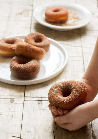 Cinnamon donuts in children's hands and on a wooden table. Selective focus.の写真素材