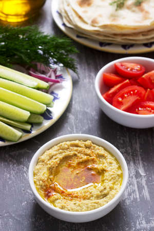 Vegan food, homemade hummus with flatbread, vegetables and olive oil on a concrete background....