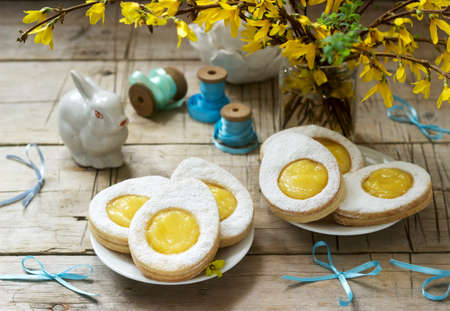 Easter composition with egg-shaped cookies filled with lemon curd, rabbit, bouquet of forsythia and...