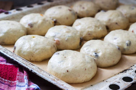 Baking tray with round uncooked cross buns on a wooden table. Selective focus.