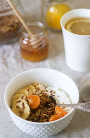 Breakfast of granola with yogurt and tea and forsythia flowers on a linen tablecloth. Rustic style,...