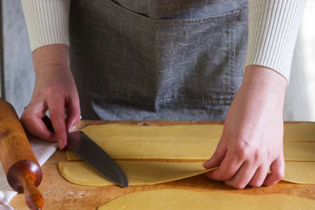 A woman makes homemade noodles from flour, eggs and salt. Rustic style, selective focus.
