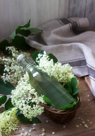 Homemade syrup of elderberry flowers in a glass jar and elder branches on a wooden table Rustic style, selective focus.の写真素材