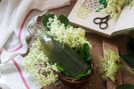Homemade syrup of elderberry flowers in a glass jar and elder branches on a wooden table Rustic style, selective focus.の写真素材