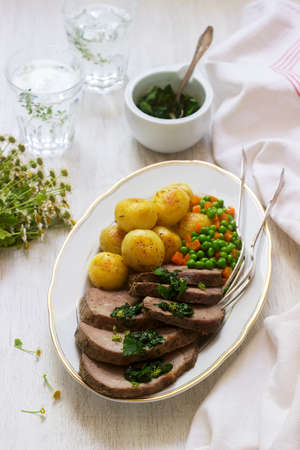 Slices of baked meat with potatoes and a garnish of peas and carrots on light background.の写真素材