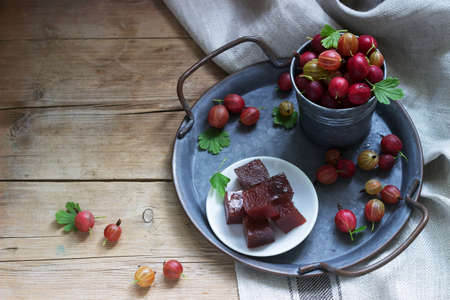 Gooseberry marmalade cubes and gooseberries on a tin tray. Rustic style, selective focus.