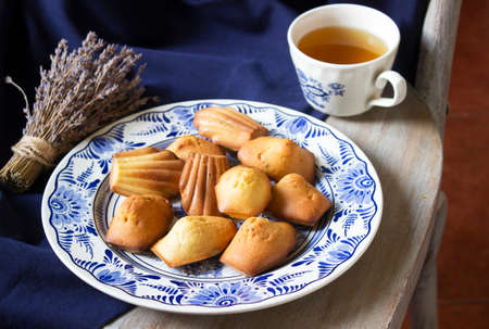 Lavender madeleines on a porcelain plate on a blue background. Rustic style.