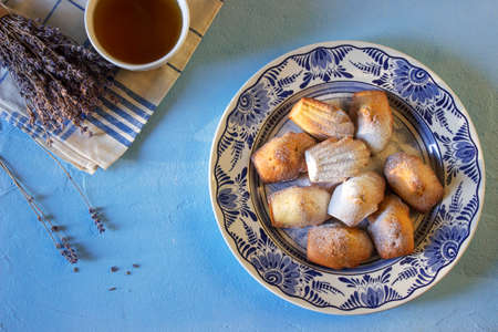 Lavender madeleines on a porcelain plate on a blue background. Rustic style.