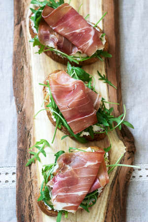Traditional italian appetizer bruschetta of toasted bread with cottage cheese, arugula and prosciutto. Selective focus.の写真素材