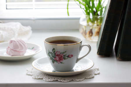 Tea in a vintage cup, marshmallows on a vintage saucer and old books on a light background.