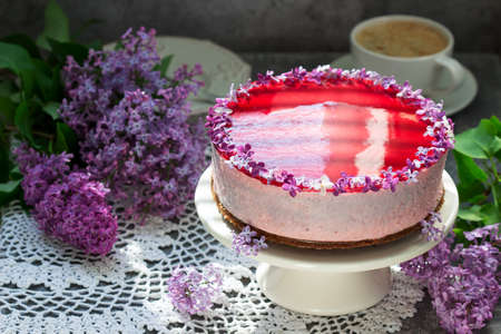 A berry mousse cake with chocolate base and juice jelly, decorated with lilac flowers, served with...
