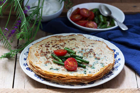 Nettle and spinach pancakes served with sour cream sauce, tomatoes and asparagus. Rustic style, selective focus.の写真素材