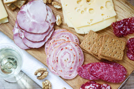 Appetizer of various types of sausages, meats, cheeses and crackers on a wooden board, served to...