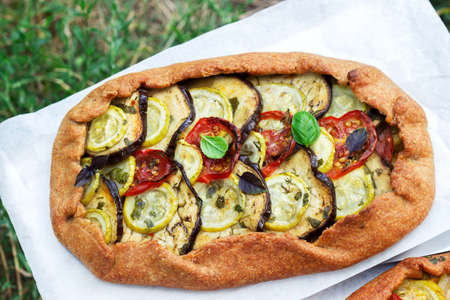 Vegetarian pies with vegetables and herbs on a stool against a background of green grass. Rustic style, selective focus.の写真素材