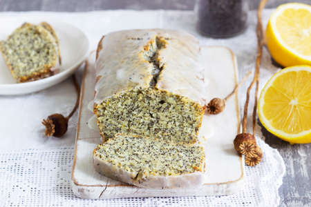 Lemon cake with poppy seeds, covered with glaze on a light background.