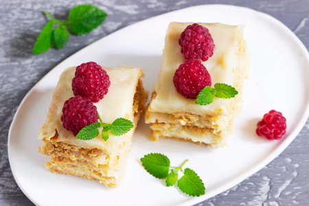 Pieces of Napoleon cake decorated with raspberries and lemon balm leaves on a light background.の写真素材