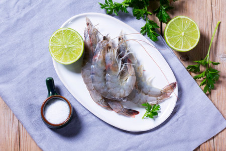 Fresh shrimp, lime, salt, and parsley on a ceramic plate on a wooden table.