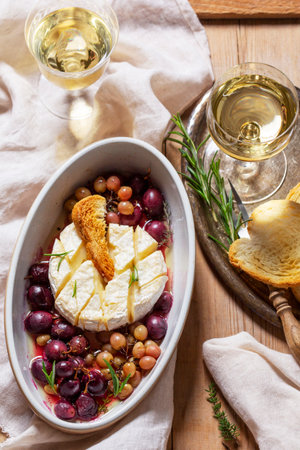 Baked Camembert cheese with grapes, thyme, and rosemary, served with white wine and a baguette.の写真素材