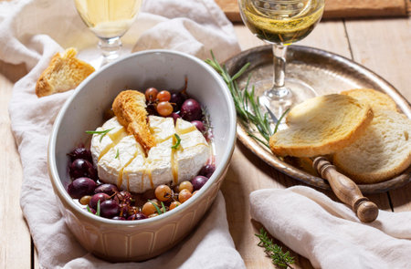 Baked Camembert cheese with grapes, thyme, and rosemary, served with white wine and a baguette.の写真素材