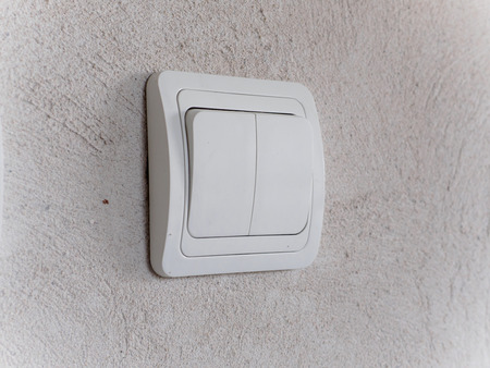 Modern white light switch on gray concrete wall. Copyspace for text.
