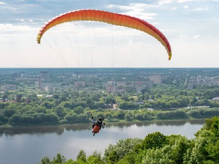 Paraglider flying over the big city. Wide river and green trees id on the background. Copyspace for...