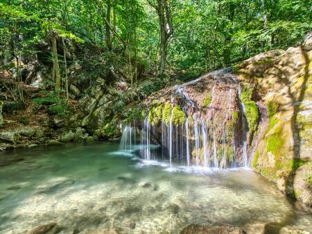 Small waterfall on the river in the mountains. Deep forest on the shores of river with stones and rocks.の写真素材