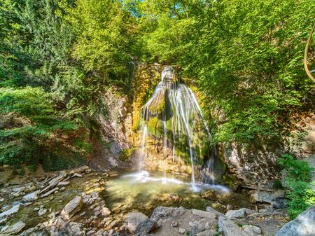 Small waterfall on the river in the mountains. Deep forest on the shores of river with stones and rocks.の写真素材