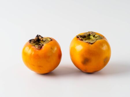 Two persimmon isolated on white background. Fresh fruit of diospyros tree that grows in tropical lands. Copyspace for text.の写真素材